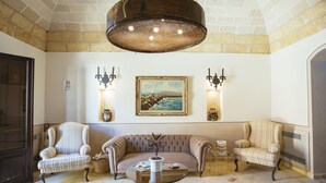 A lobby with a beige sofa, two striped armchairs, a round glass coffee table, and a painting on the wall. - Hotel Baglio Catalano (Custonaci)