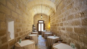 A stone-walled dining area with round tables, each with a white tablecloth and a menu card. - Hotel Baglio Catalano (Custonaci)