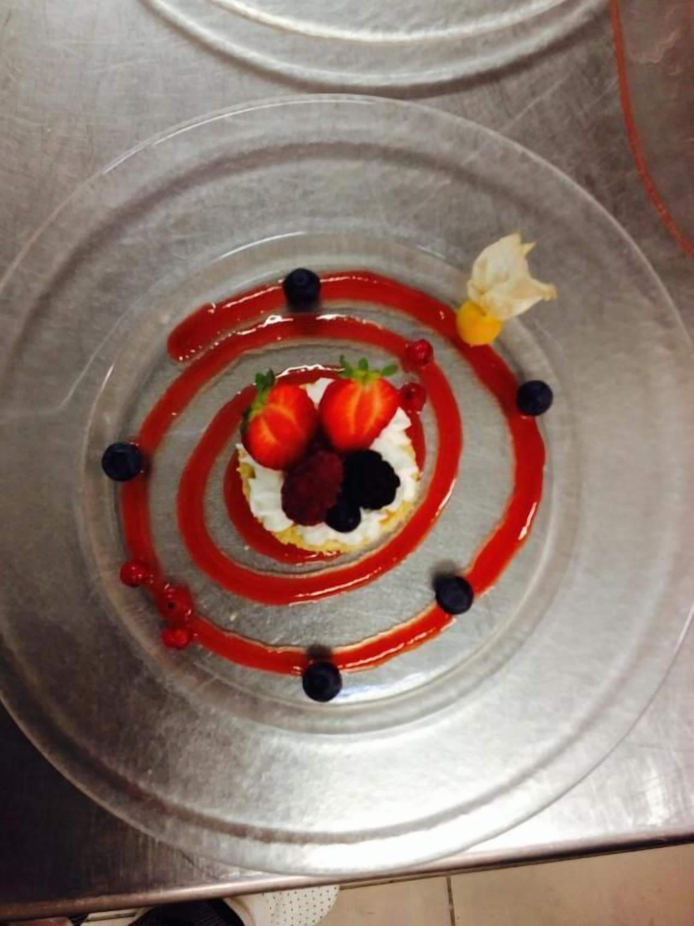 Un dessert con fragole, mirtilli e un fiore su un piatto di metallo.