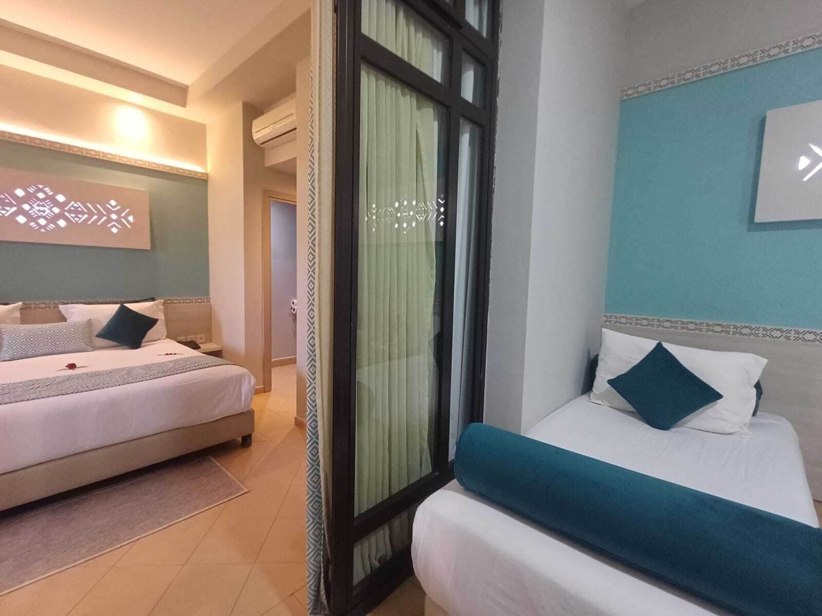 Habitación de hotel con dos camas, un ventanal con cortinas, una lámpara fijada a la pared y un adorno mural con diseño.