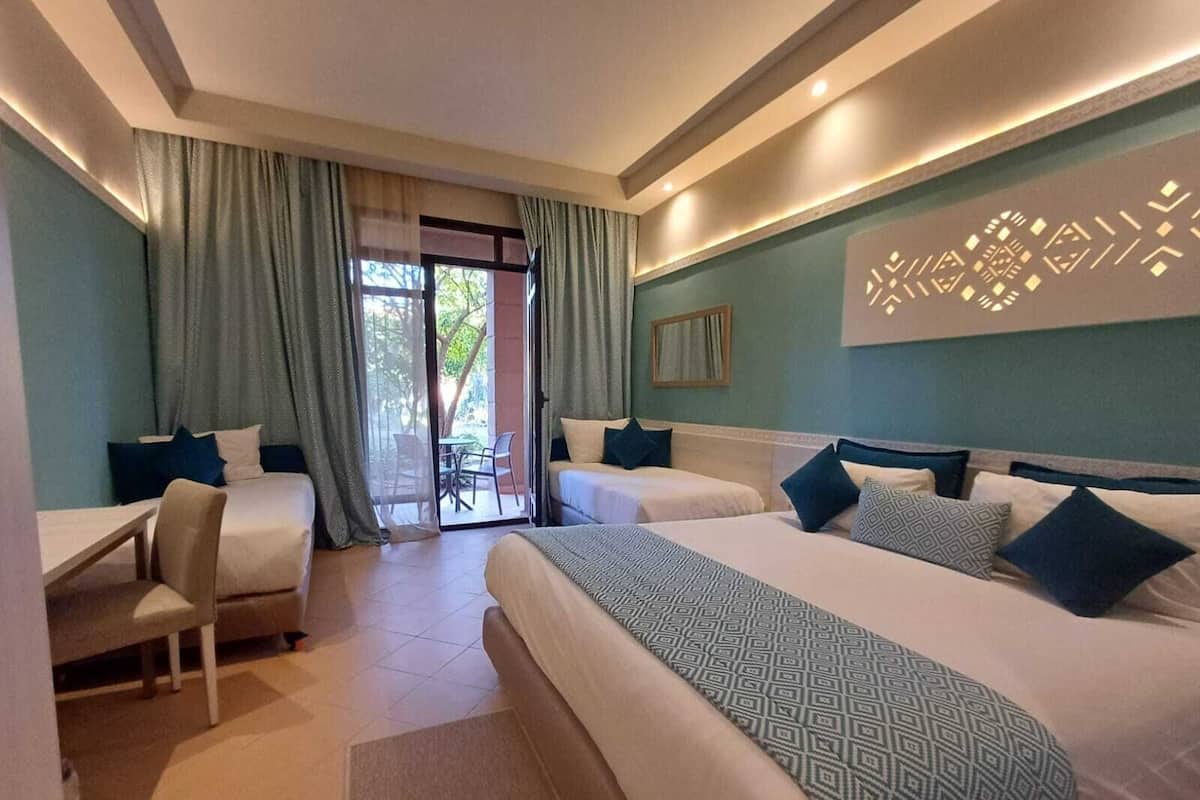 A hotel room with two beds, a desk, and a chair. There is a sliding glass door leading to an outdoor area.