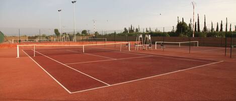 A tennis court with a net, white boundary lines, and floodlights.