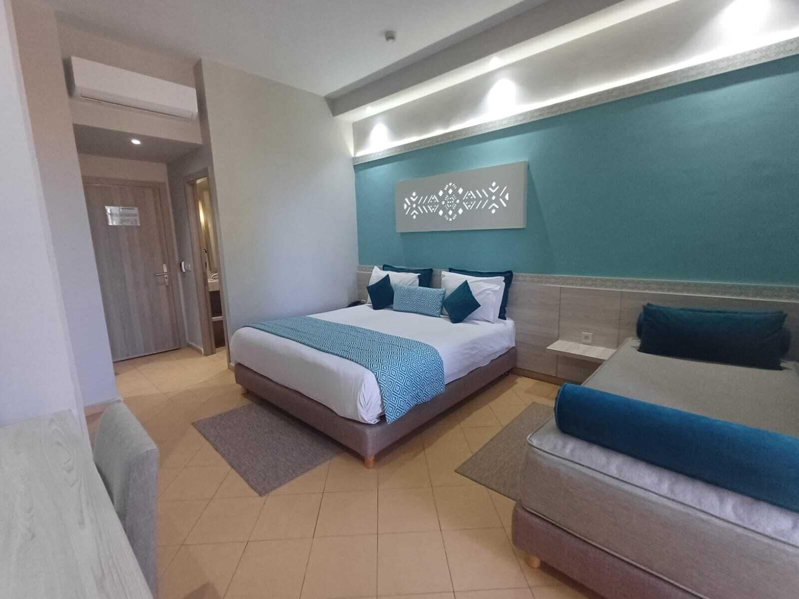 Habitación de hotel con cama, sofá, una obra de arte en la pared y puerta que da a otra estancia.