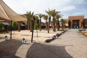 A courtyard with palm trees, a brick pathway, and a building with a modern design. - Aqua Mirage Club & Aqua Parc - All Inclusive (Marrakech)