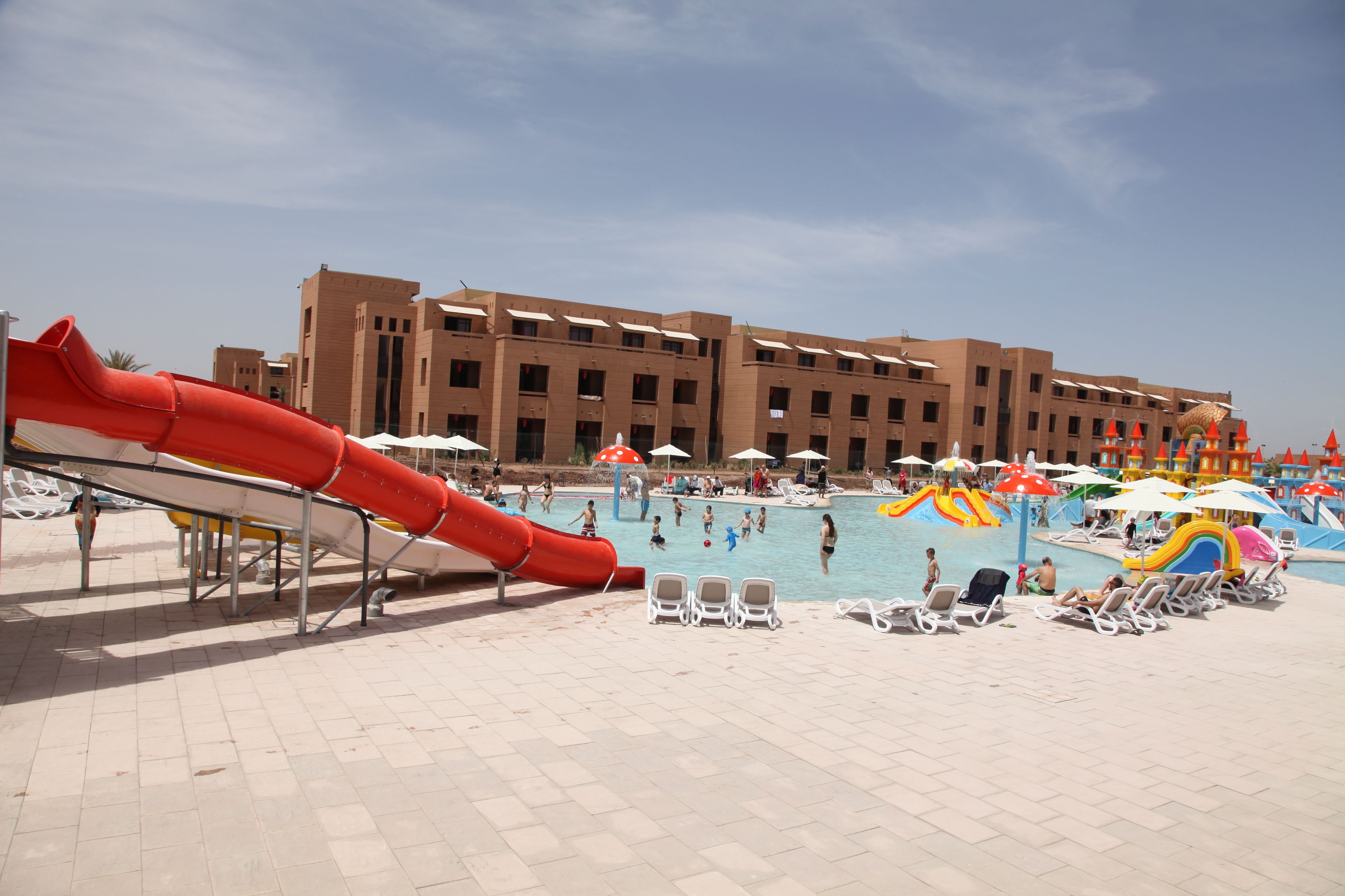 A pool area with a red slide, sun loungers, and umbrellas.
