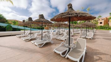 A poolside area with lounge chairs and thatched umbrellas.