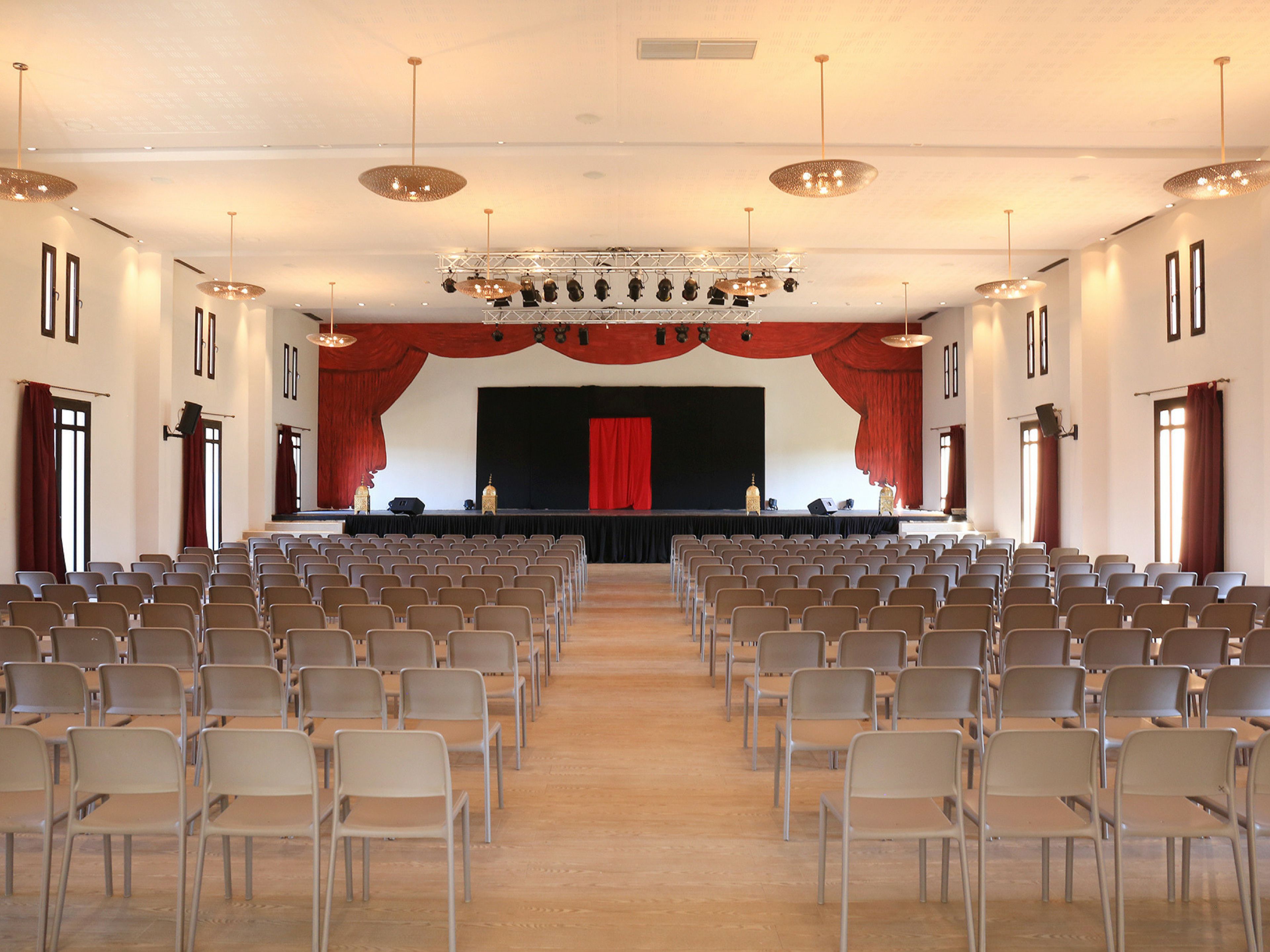 A large hall with rows of chairs facing a stage with a red curtain.