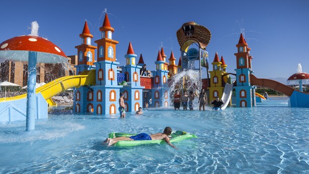 Parque acuático con una estructura tipo castillo, toboganes y una persona en un flotador.