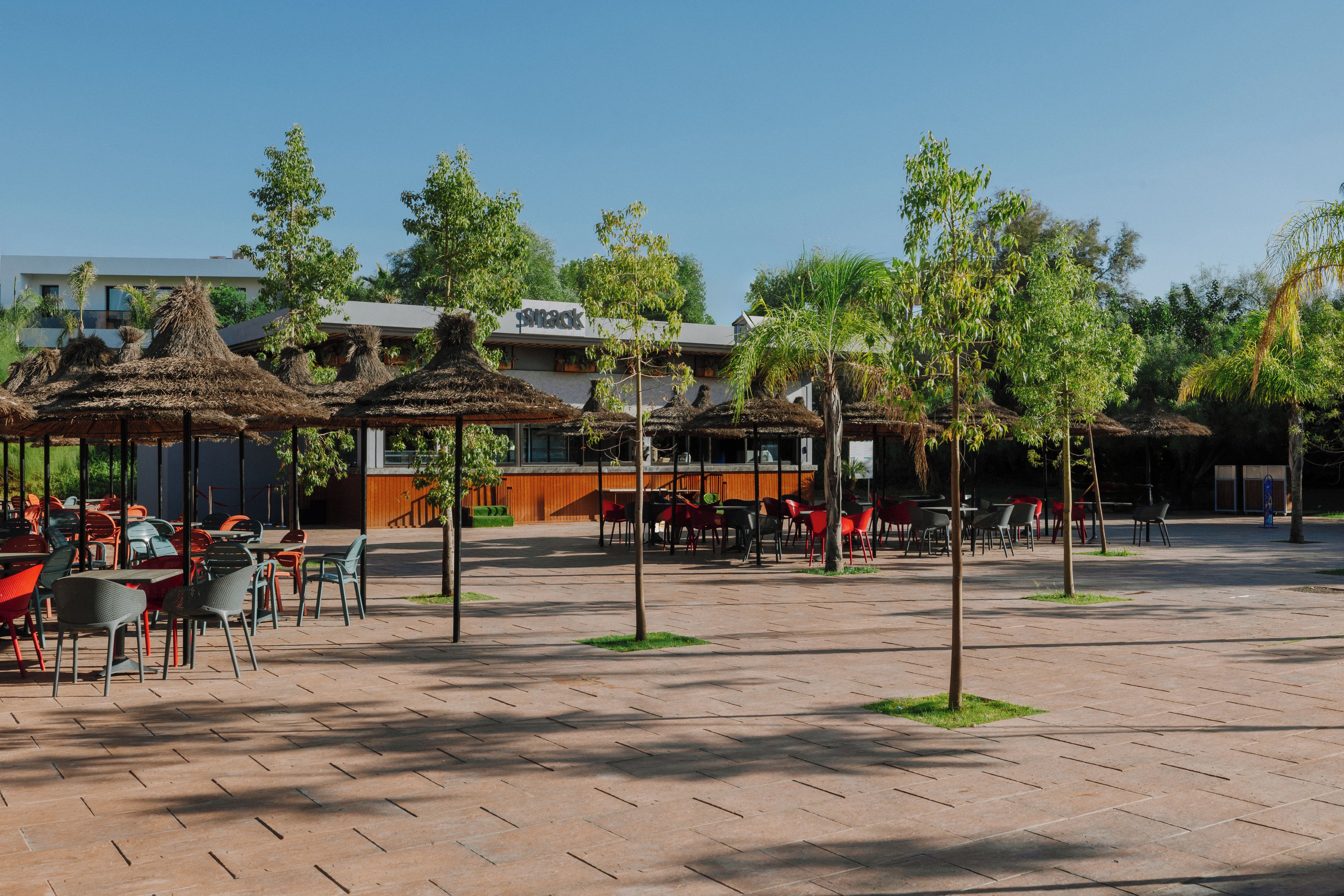 An outdoor seating area with tables and chairs, surrounded by trees and a building with a sign that reads 'snack'.