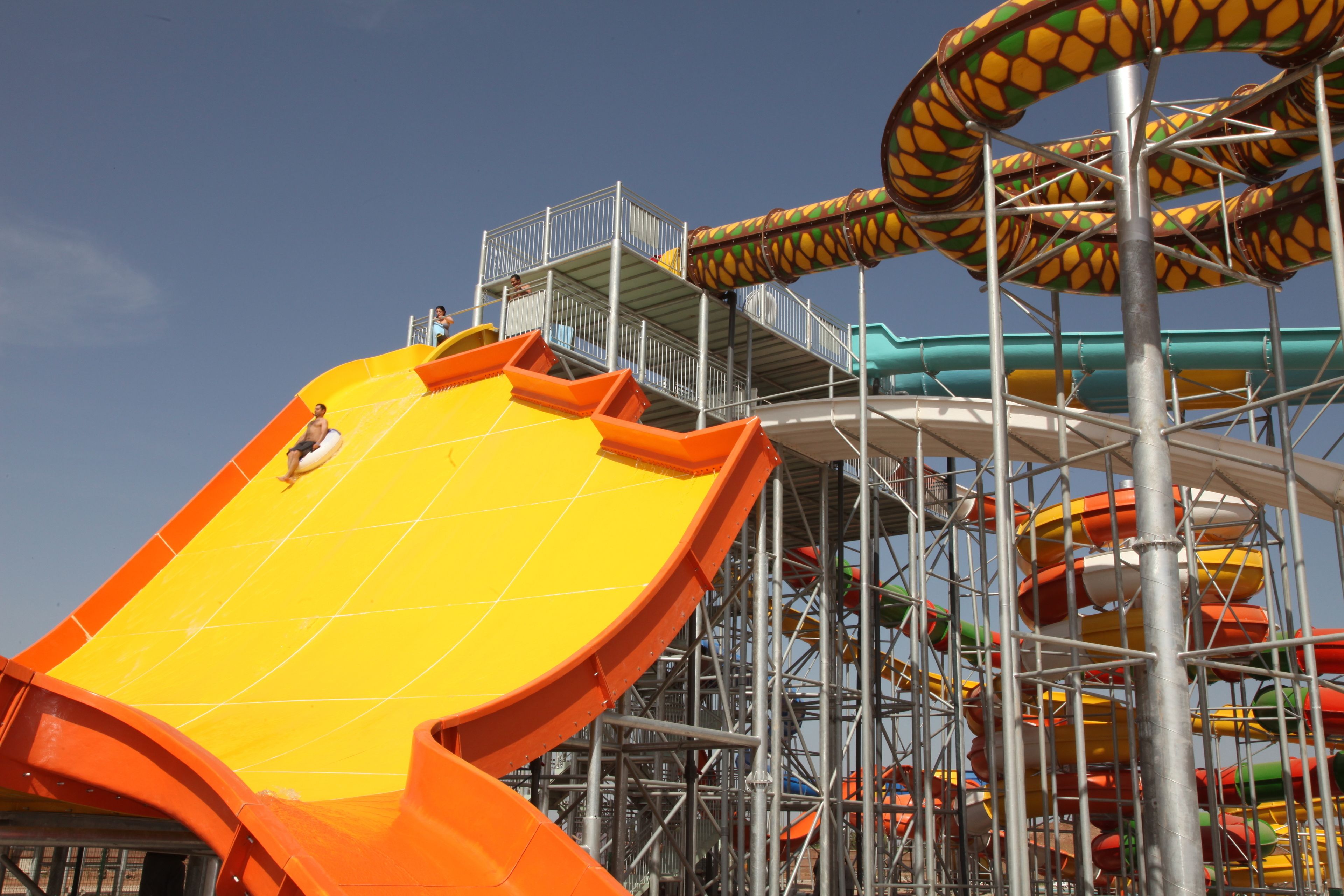 Un parque acuático con un tobogán amarillo grande, varios toboganes y una estructura de metal.