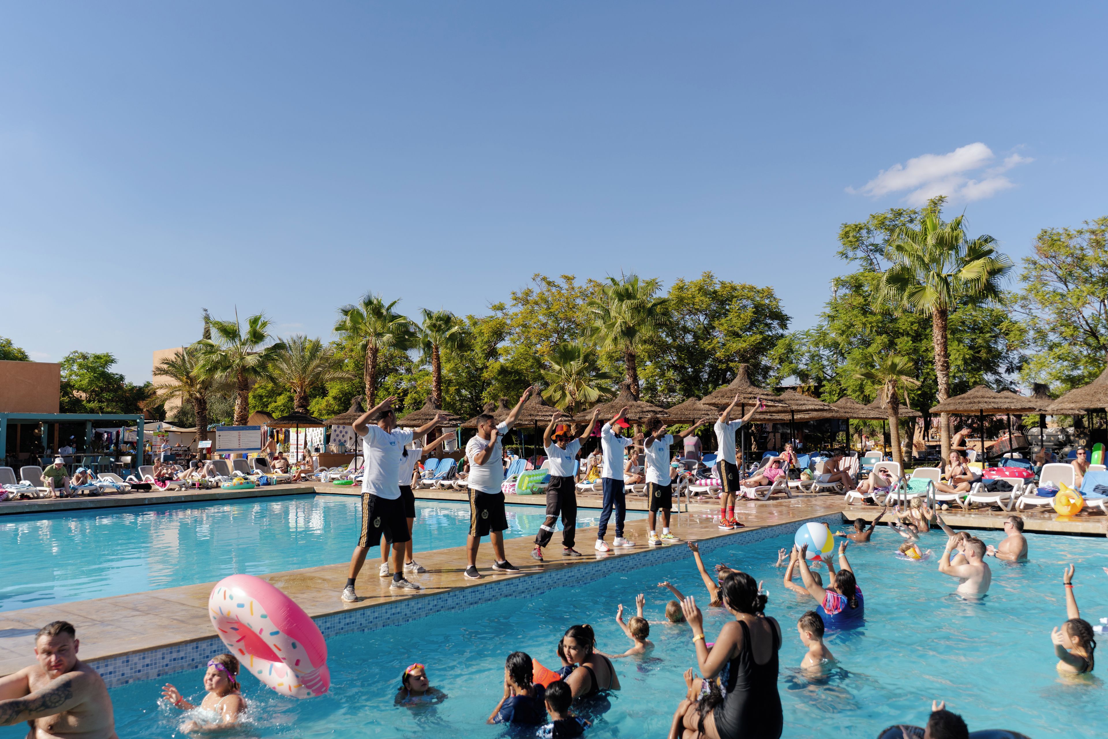 A swimming pool with people engaging in water activities and a group performing a synchronized exercise routine.