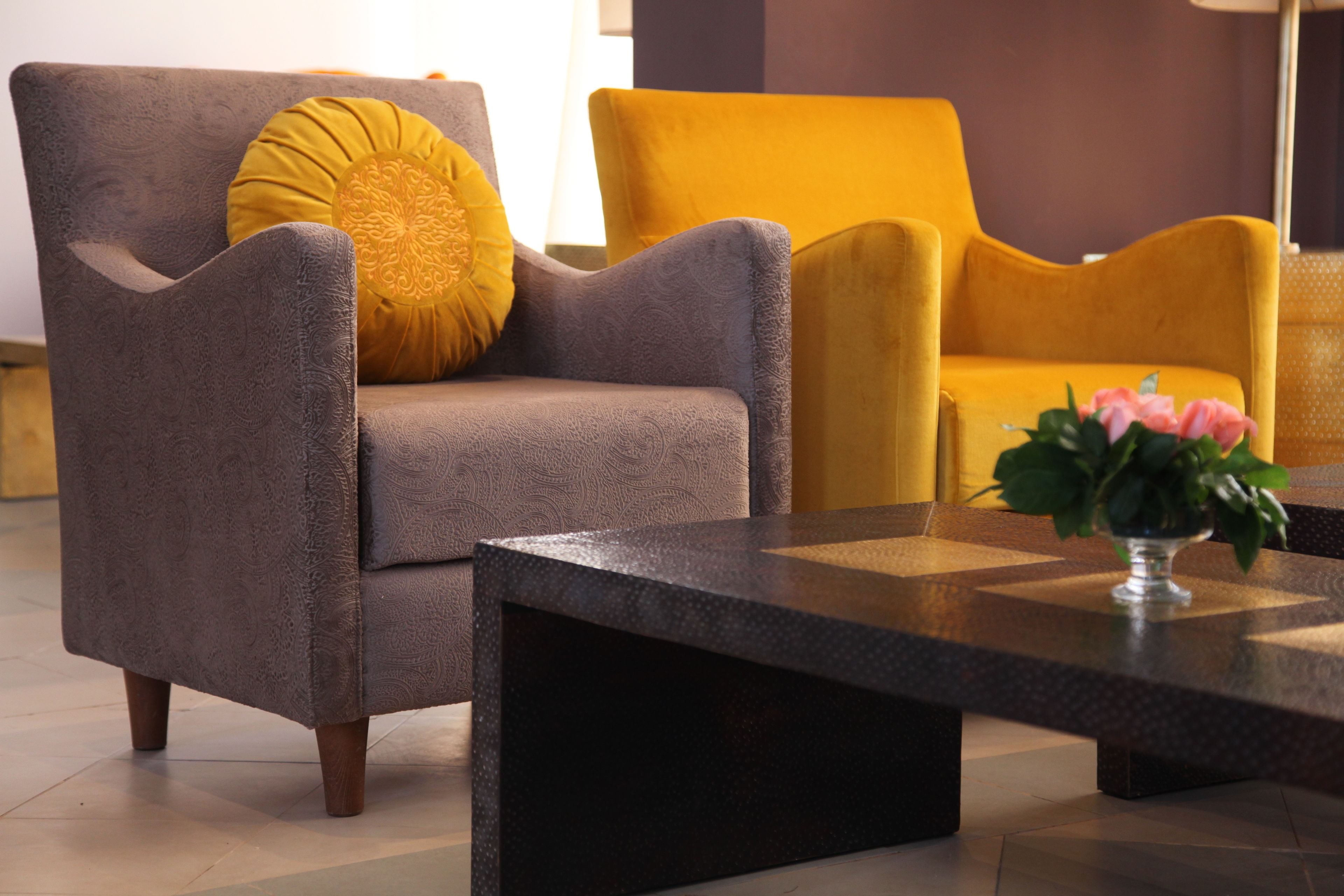 Un salon moderne avec un fauteuil gris, un fauteuil jaune et une table basse noire sur laquelle est posé un vase de fleurs.