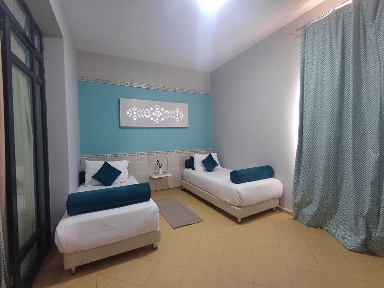 Ein Hotelzimmer mit zwei Betten, einem kleinen Nachttisch, einer Wanddekoration und einem Vorhang.