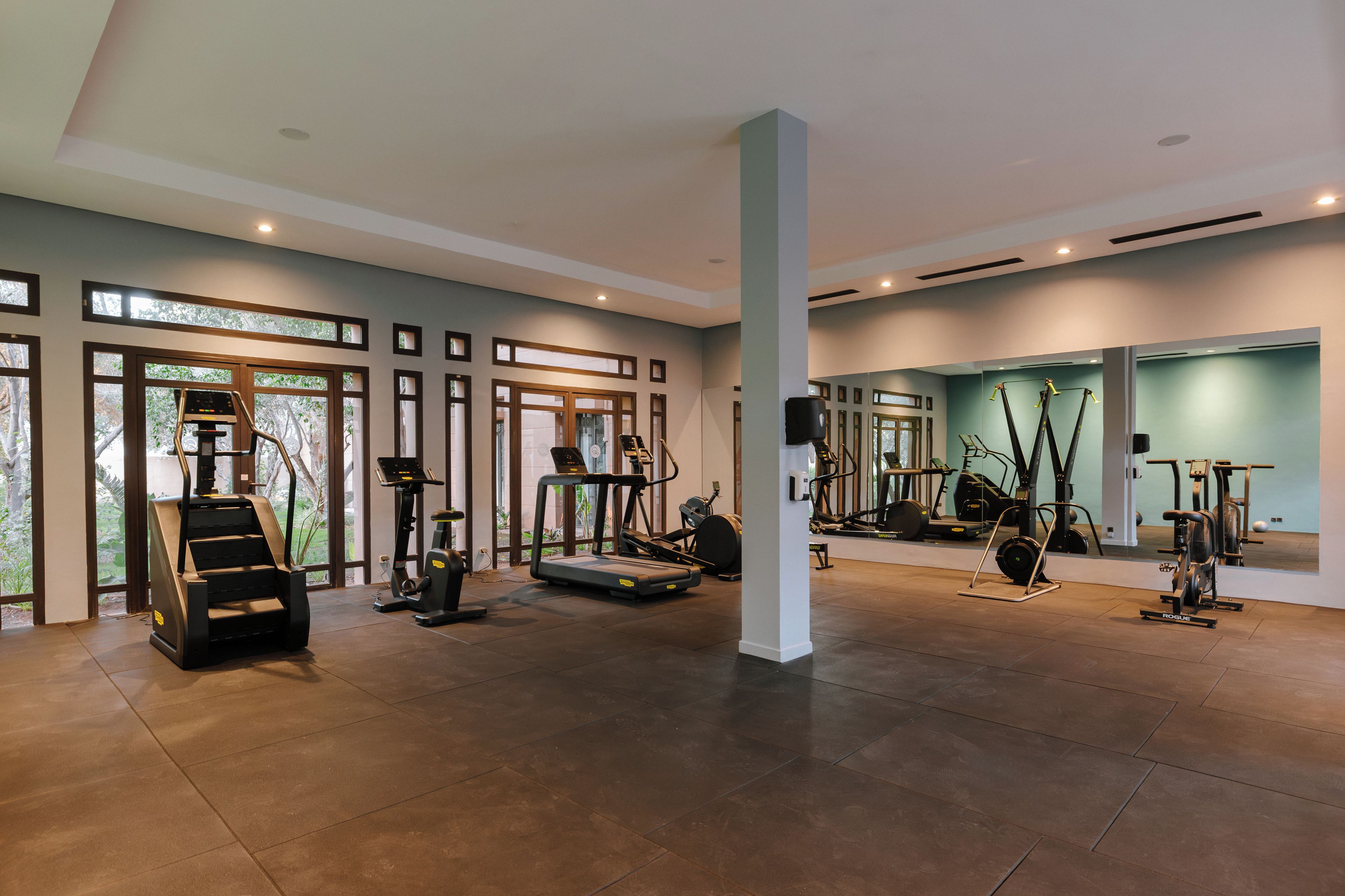 Une salle de sport spacieuse, dotée de divers appareils d’entraînement, de grandes fenêtres et d’un plafond haut.