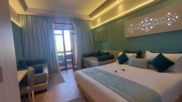 A hotel room with a large bed, a sofa, a desk, and a balcony with curtains.