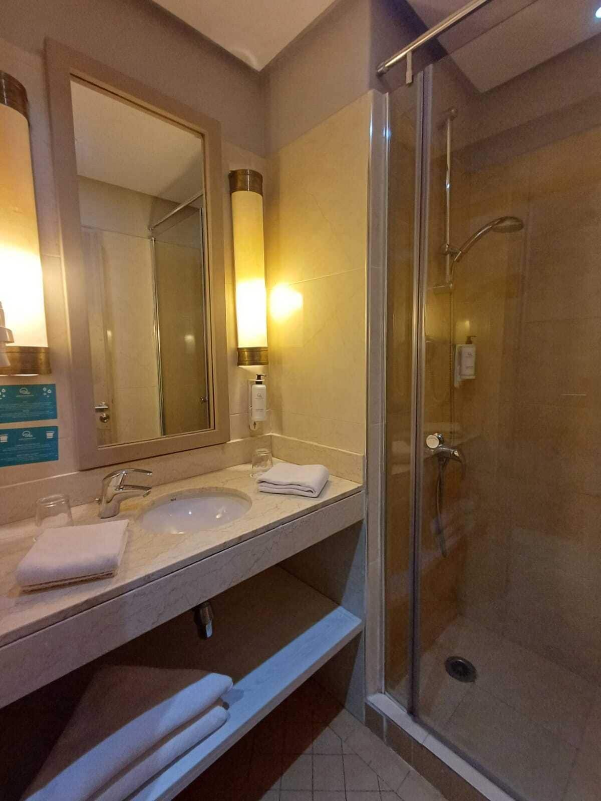 A modern bathroom with a glass-enclosed shower, a sink with a mirror, and a bench below.