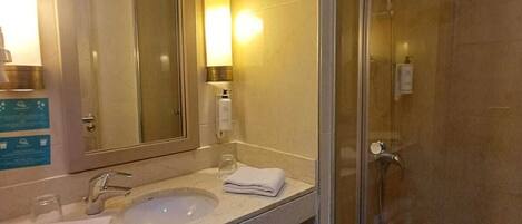 Un baño moderno con cabina de ducha de vidrio, un lavabo con espejo y una banca debajo.