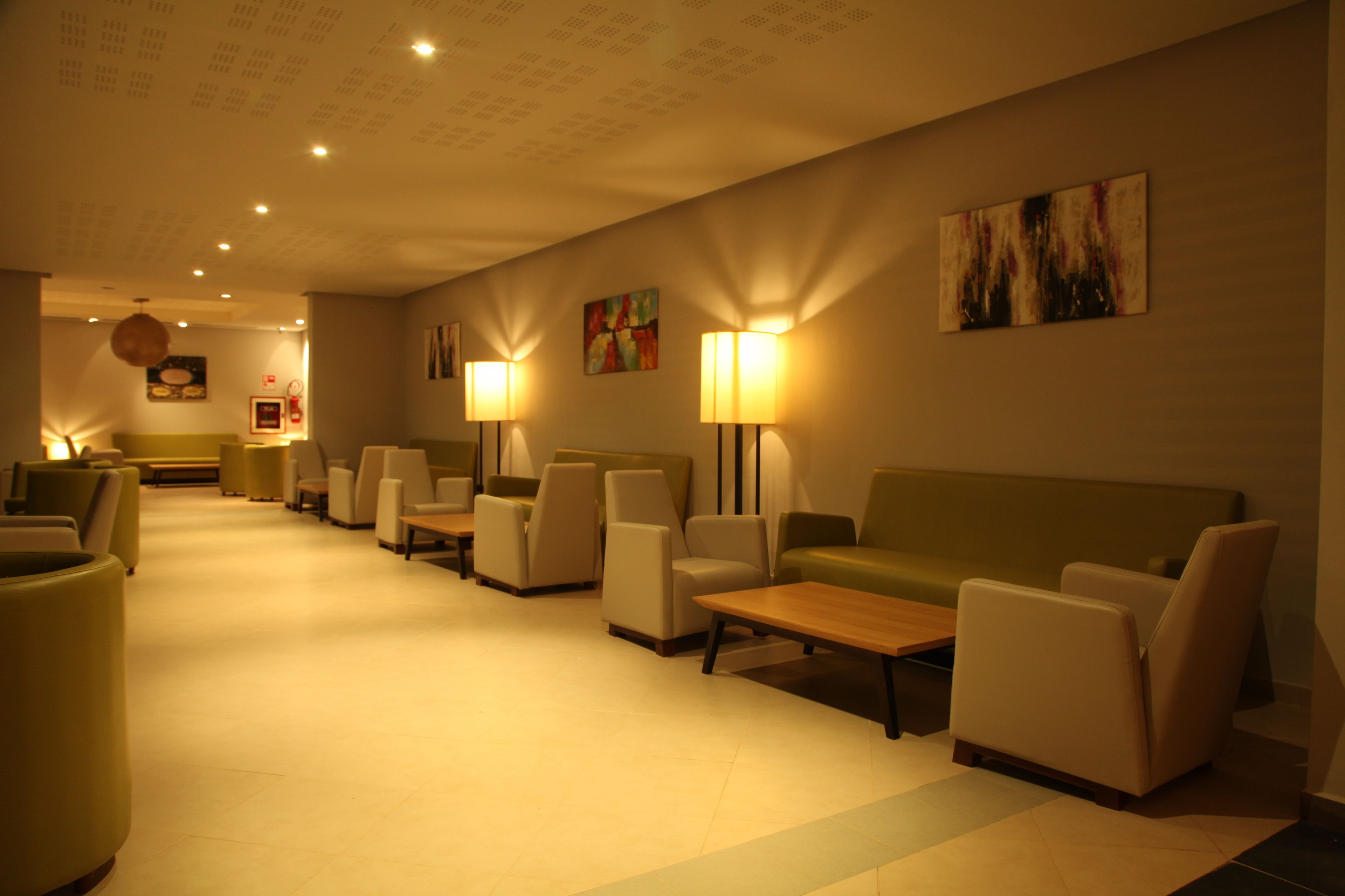 Un vestíbulo de hotel con una larga recepción, varias áreas de descanso con sofás y sillones, y lámparas fijadas a la pared.