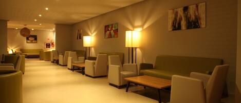Un vestíbulo de hotel con una larga recepción, varias áreas de descanso con sofás y sillones, y lámparas fijadas a la pared.