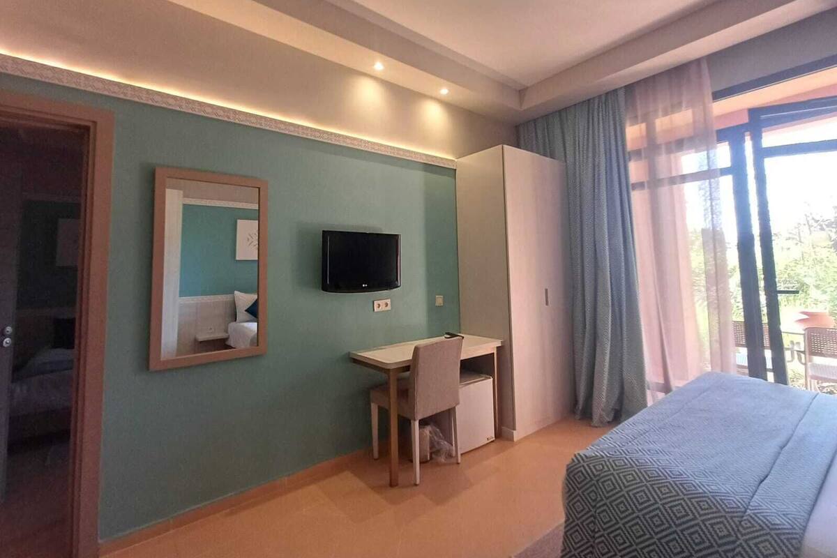 A hotel room with a bed, a desk, a television, and a wardrobe.