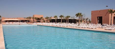 A swimming pool with lounge chairs and palm trees.