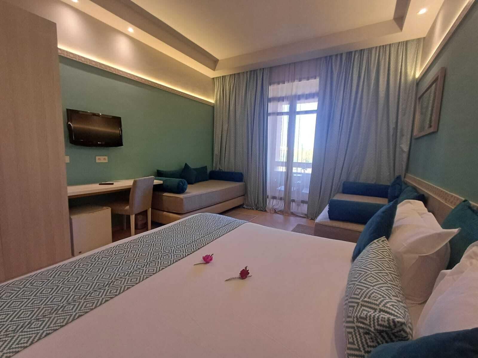 A hotel room with a bed, a desk, a chair, a television, and a large window with curtains.