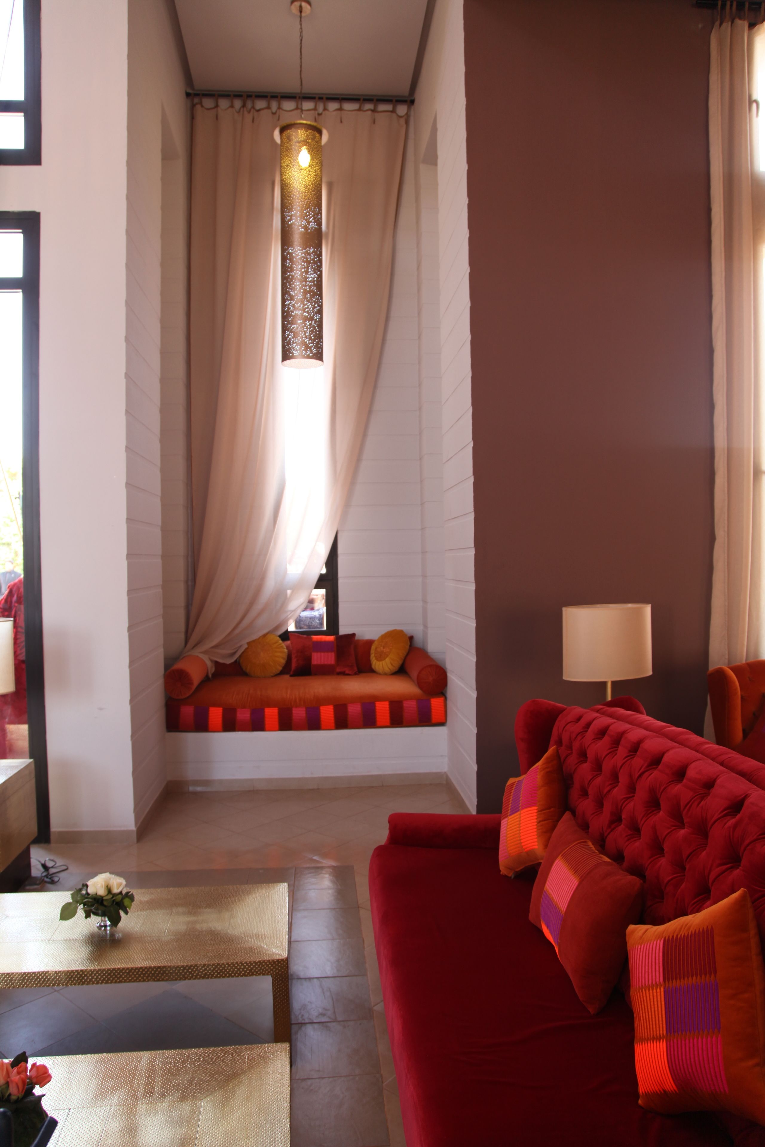 A cozy living room with a red sofa, a small table with a vase, and a window with curtains.
