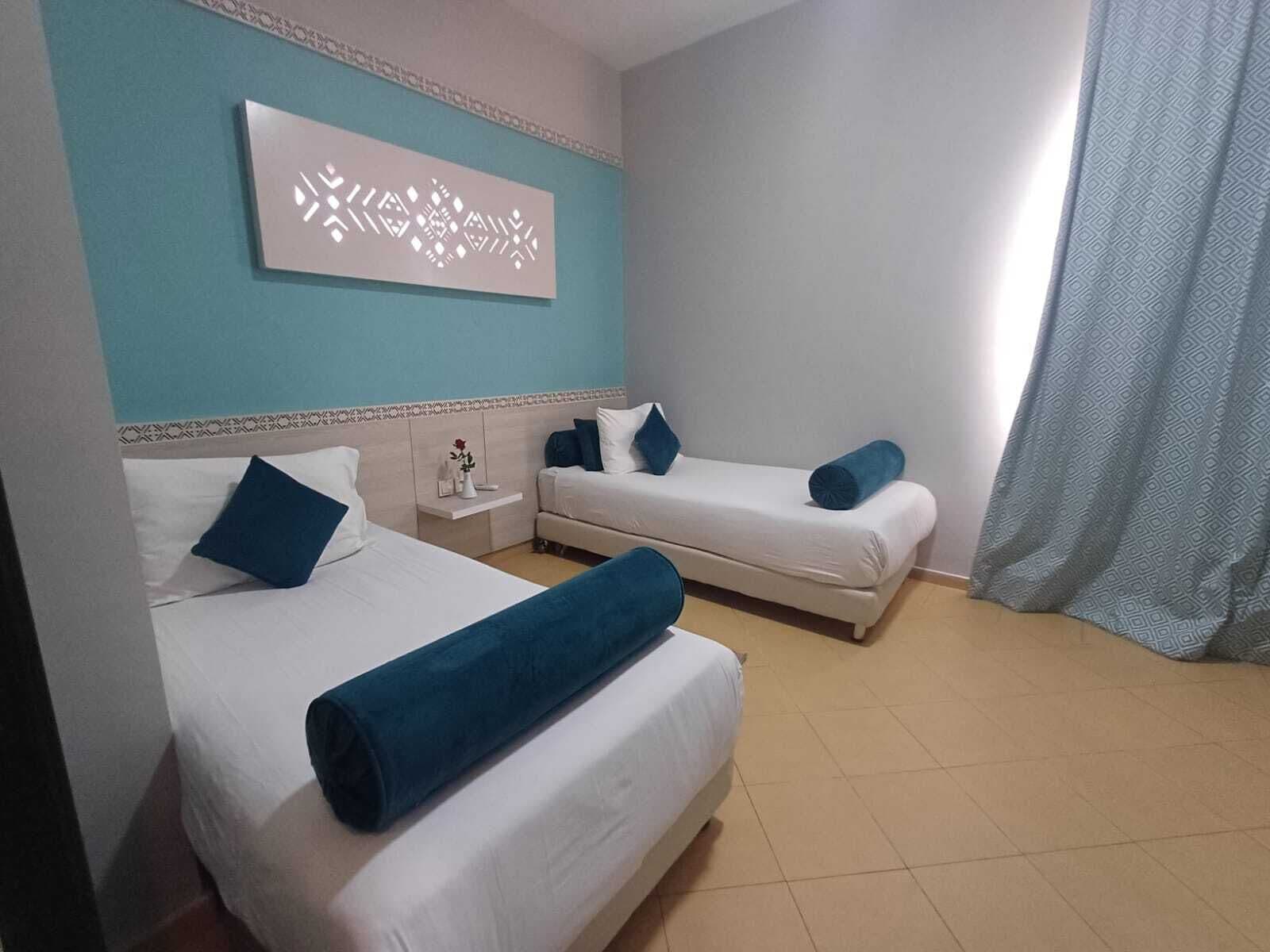 A hotel room with two beds, a nightstand, a decorative wall piece, and a curtain.