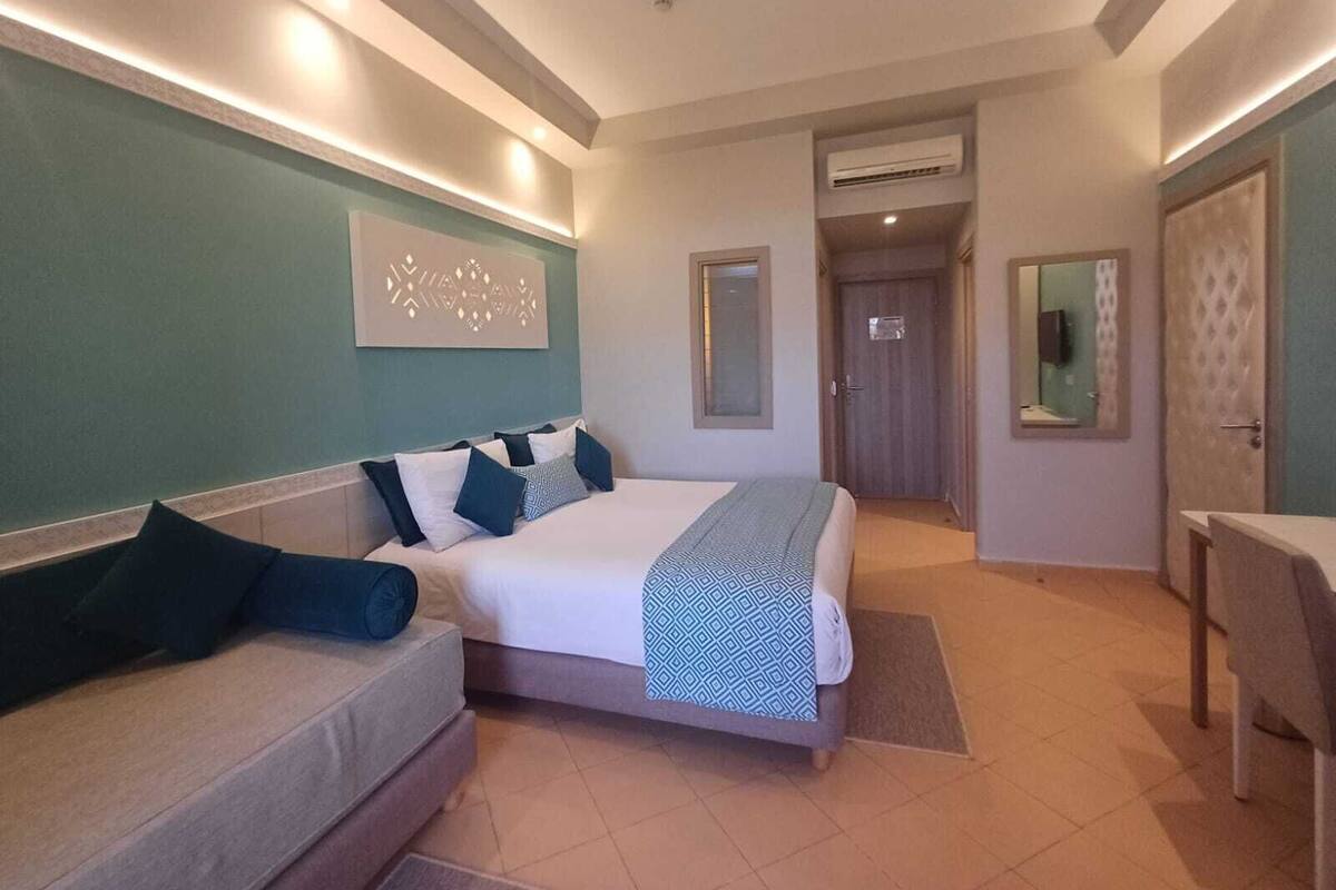 A hotel room with a bed, a sofa, a desk, and a bathroom door.