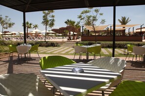 An outdoor seating area with tables and chairs, a pool, and palm trees. - Aqua Mirage Club & Aqua Parc - All Inclusive (Marrakech)