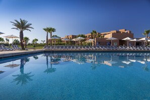 A pool with lounge chairs and umbrellas, surrounded by palm trees and buildings. - Aqua Mirage Club & Aqua Parc - All Inclusive (Marrakech)