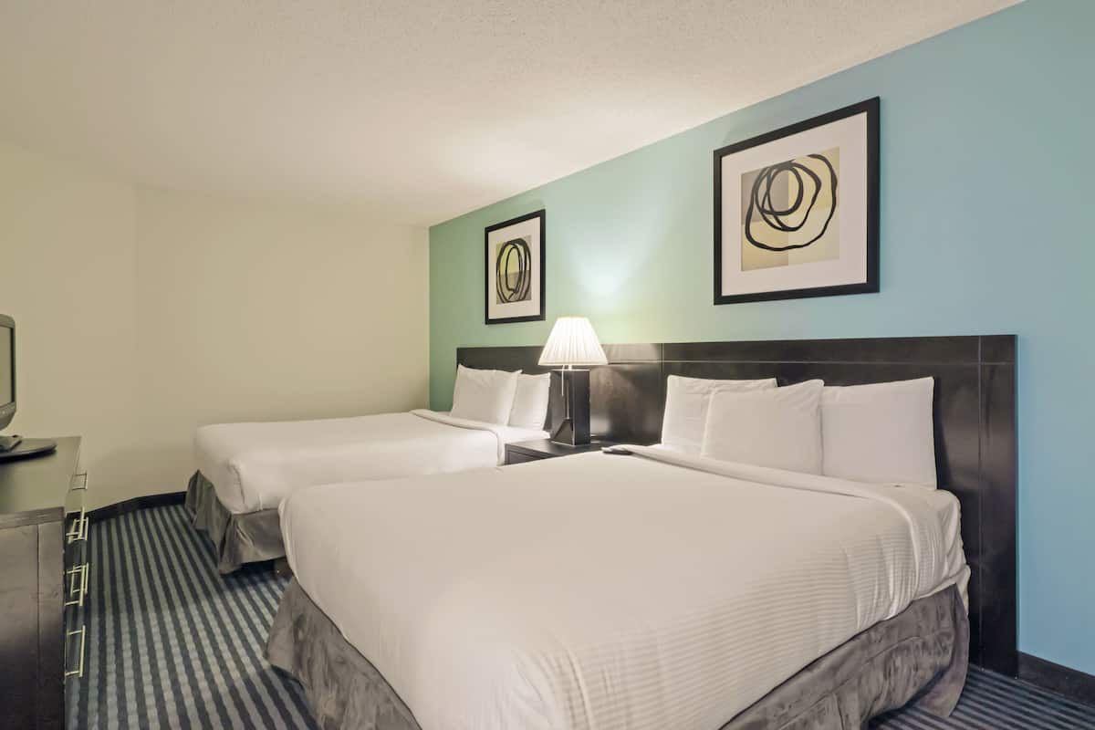 A hotel room with two beds, a nightstand with a lamp, a TV, and artwork on the walls.