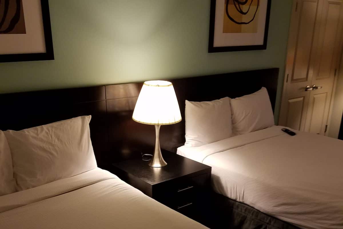 A hotel room with two beds, a bedside table with a lamp, and artwork on the walls.