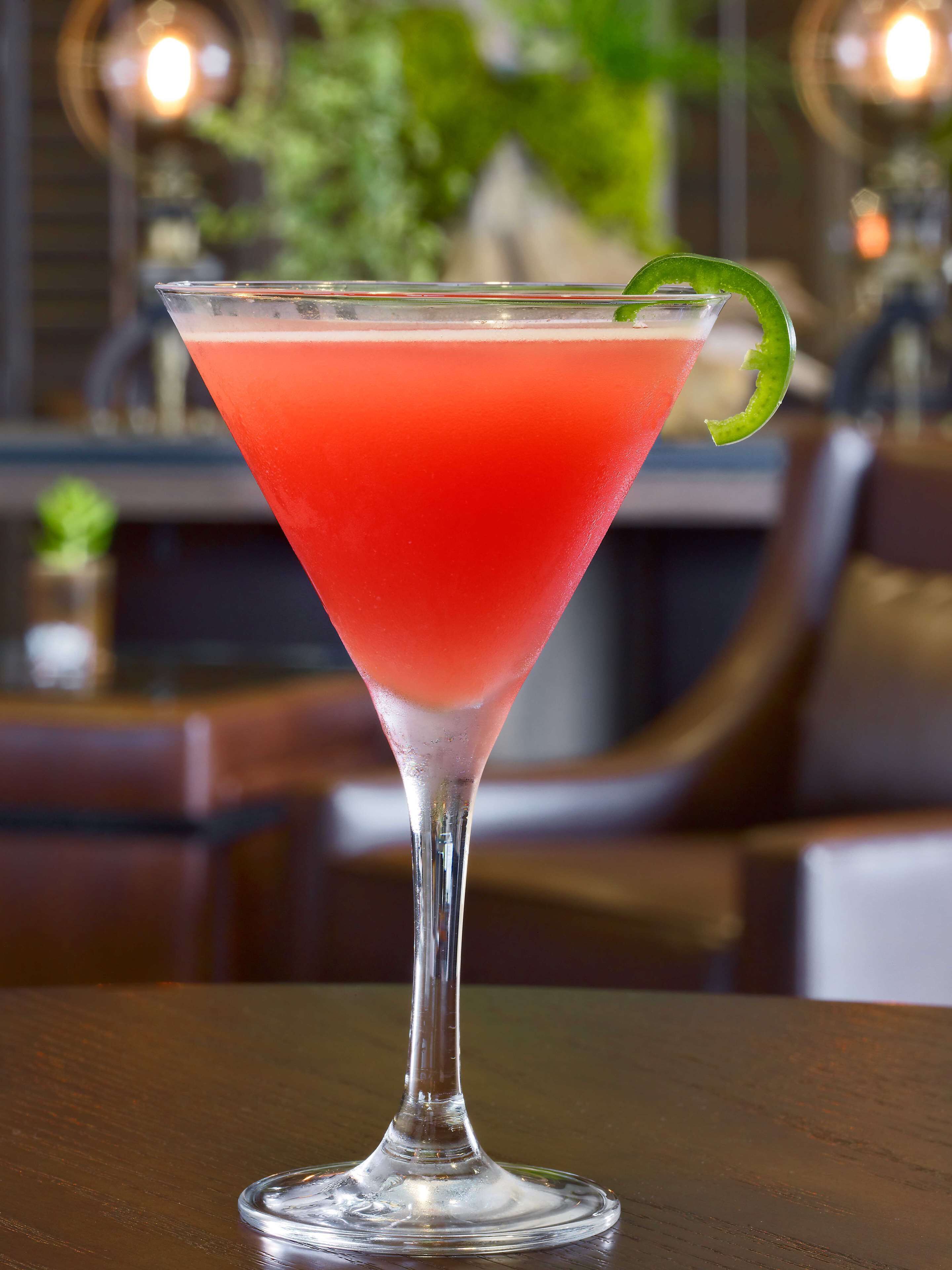 Ein Cocktail im Martiniglas mit Limettenscheibe auf einer Holztischplatte.