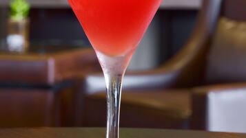 Ein Cocktail im Martiniglas mit Limettenscheibe auf einer Holztischplatte.