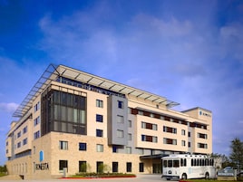 A modern hotel building with multiple floors, large windows, and a bus parked in front.