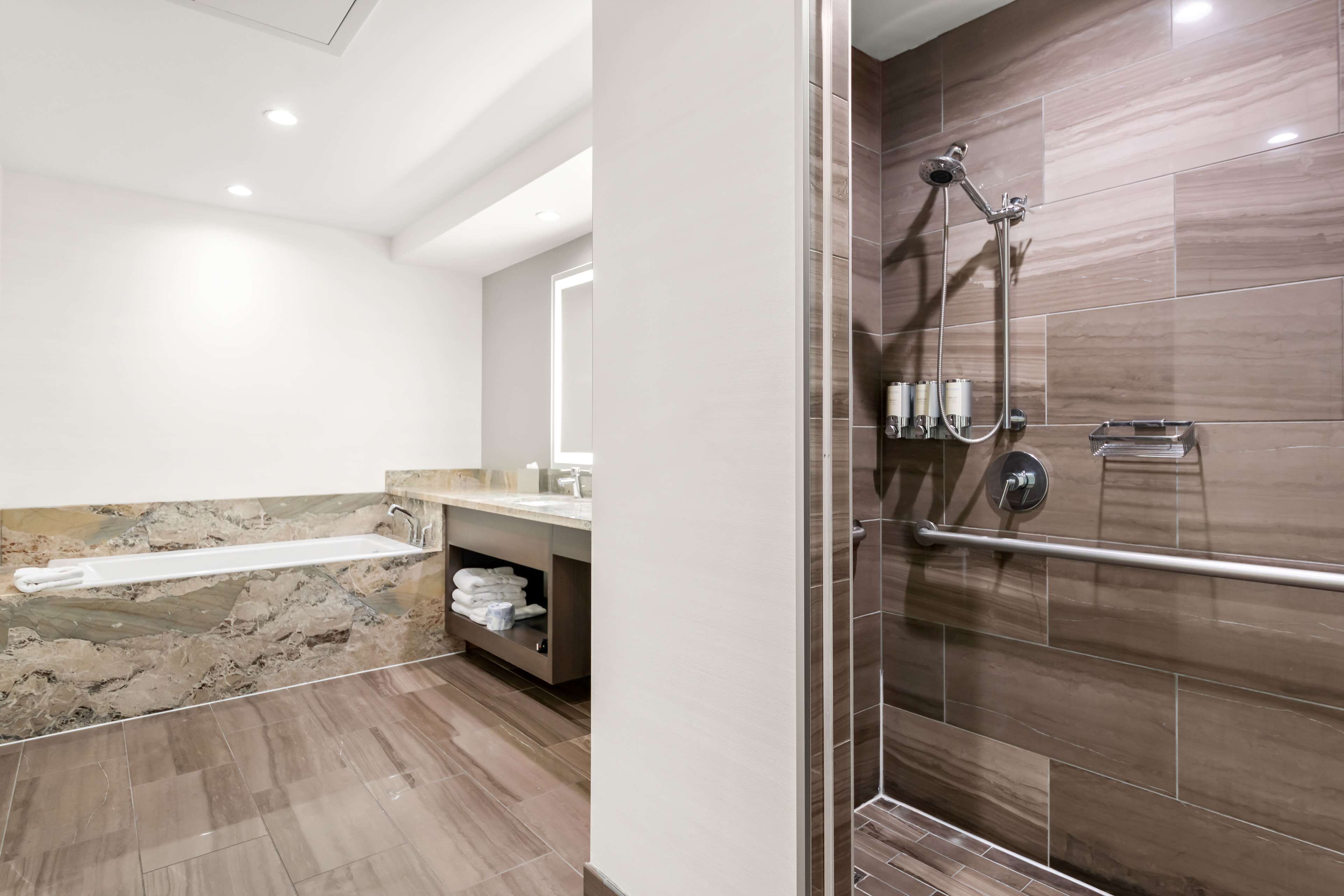 Une salle de bain moderne dotée d’une douche à parois de verre, d’un lavabo en marbre et d’une étagère intégrée où sont rangées les serviettes.