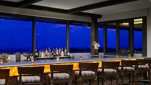 A bar area with a long counter, multiple bottles, glasses, and chairs. - Sonesta Bee Cave Austin Hill Country (Austin)