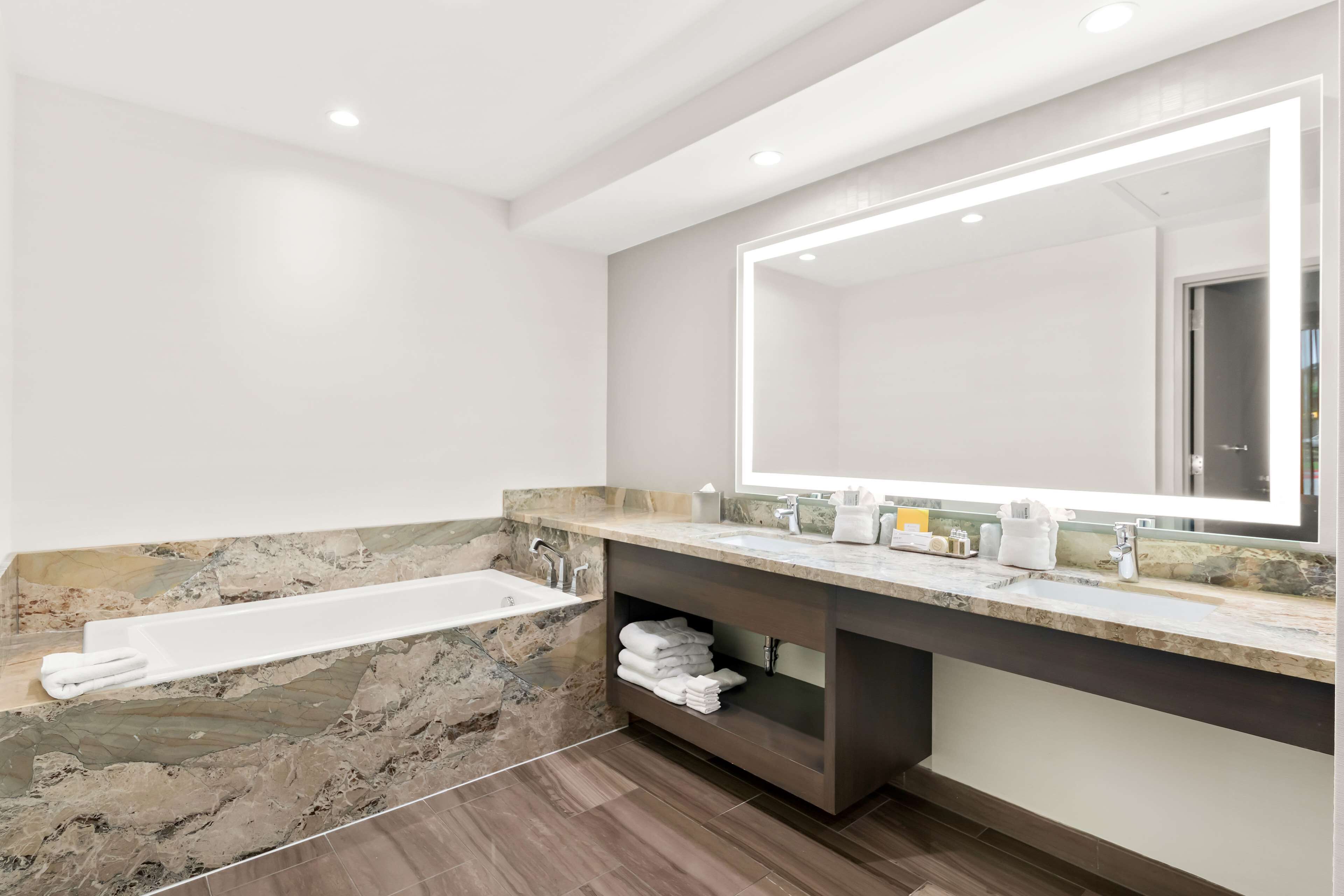A modern bathroom with a marble sink, a large mirror, and a built-in shelf with towels.
