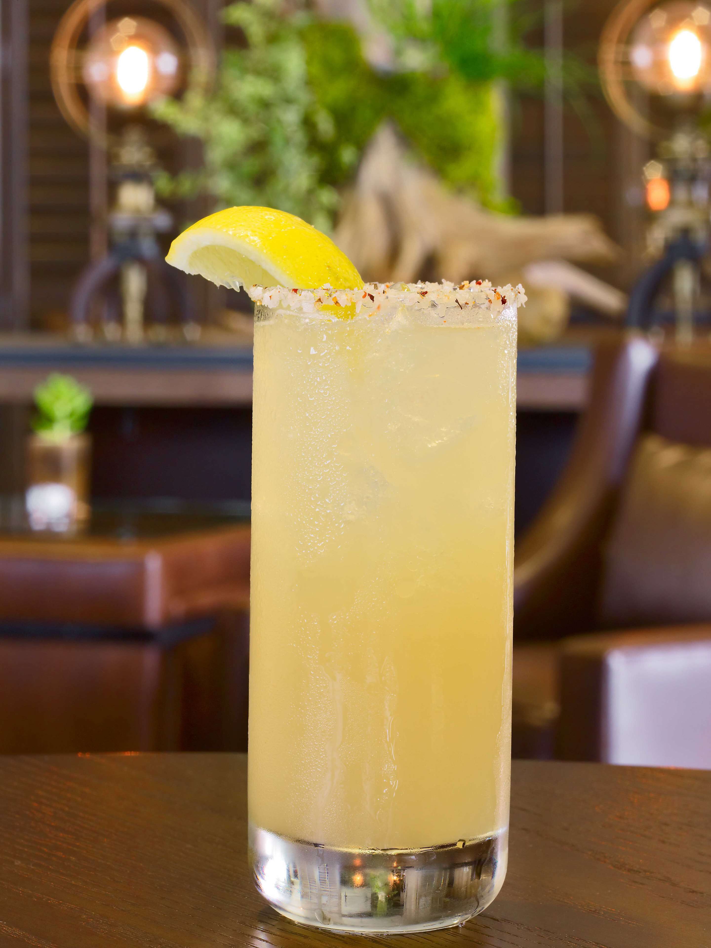 Un grand verre à bordure salée, une tranche de citron et un liquide transparent, vraisemblablement un cocktail, posés sur une table en bois.