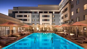 A swimming pool with lounge chairs and umbrellas, surrounded by a building with multiple floors and balconies. - Sonesta Bee Cave Austin Hill Country (Austin)