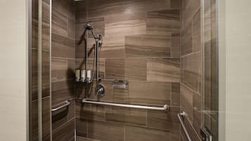 A shower with a handrail, a handheld showerhead, and a wall-mounted faucet.