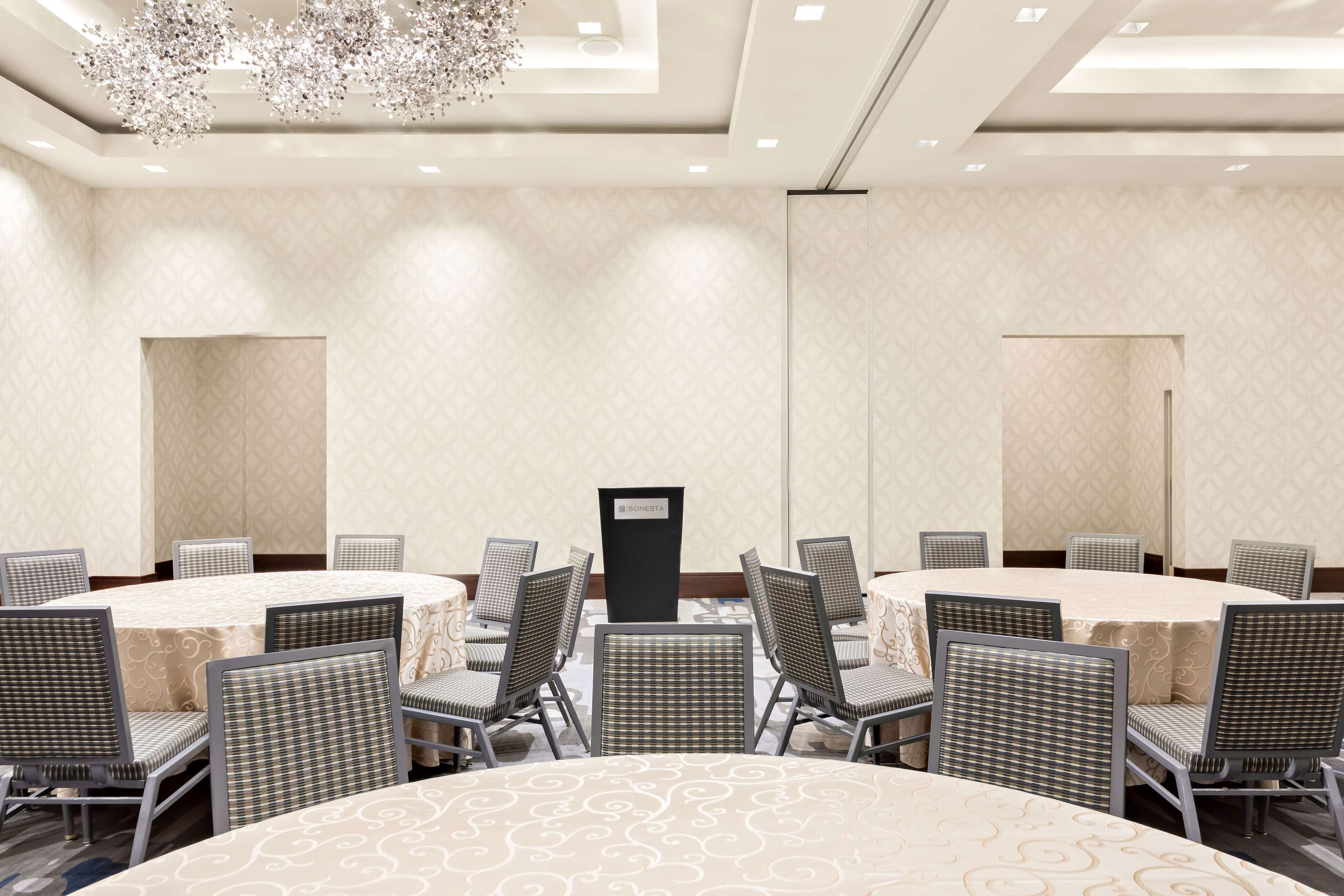 A conference room with round tables and chairs, a podium, and a chandelier.