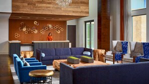 A modern lobby with a wooden ceiling, a reception desk, blue sofas, and a large chandelier. - Sonesta Bee Cave Austin Hill Country (Austin)