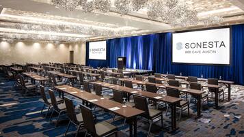 A conference room with rows of tables and chairs, a large screen displaying the SONESTA logo, and a blue curtain backdrop.