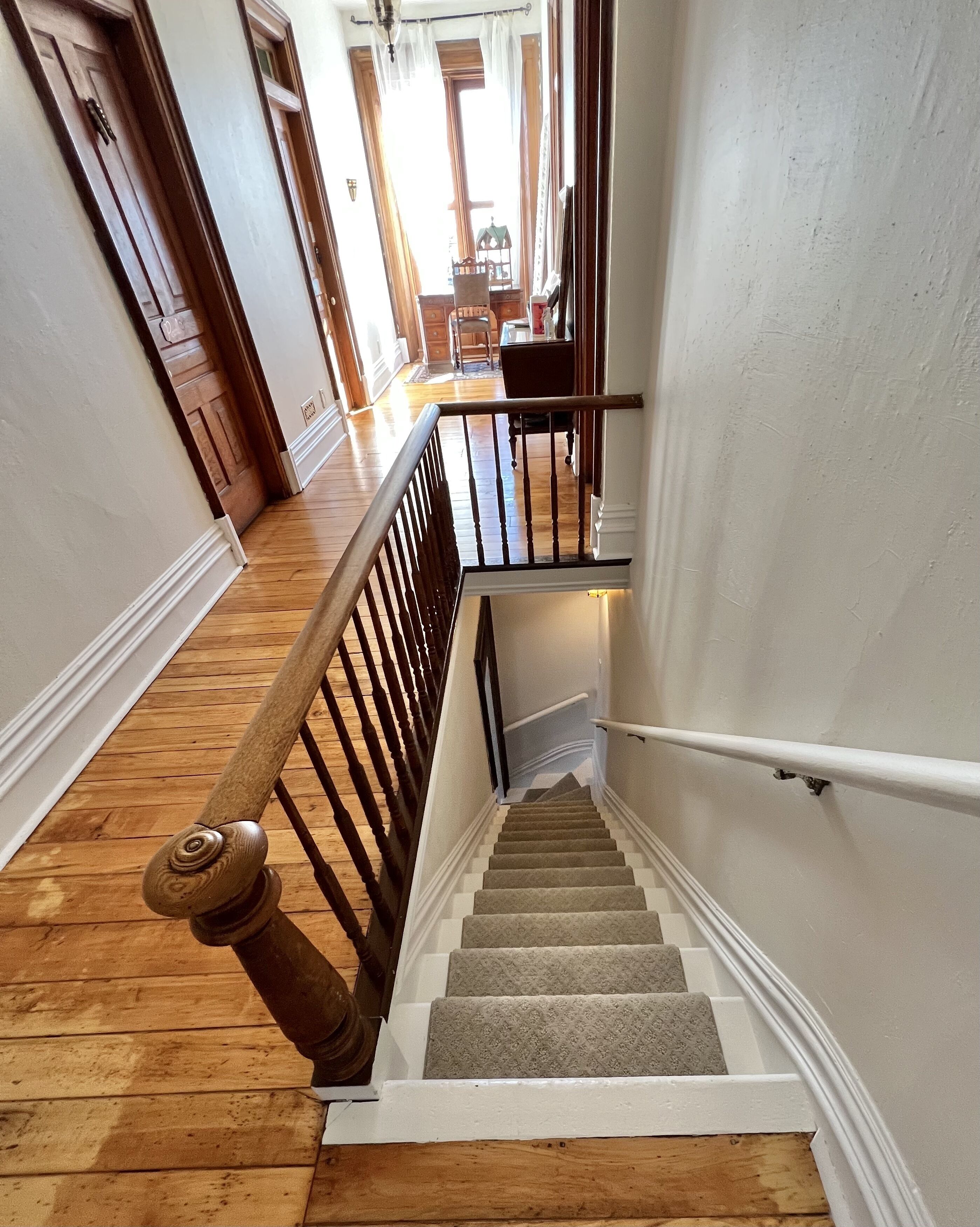 Un escalier avec des rampes en bois et des marches recouvertes de moquette, menant à l’étage supérieur.
