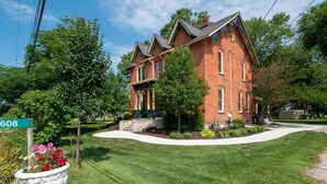 A two-story brick house with a front porch, a stone foundation, and a well-maintained lawn. - The Woodbridge House (Kingsville)
