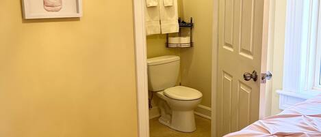 Un dormitorio con una cama, una puerta que da a un baño y dos cuadros con motivos florales en la pared.