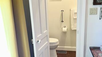 Een badkamer met een wit toilet, een douche, een handdoekhouder en een klein tafeltje met een decoratief object.