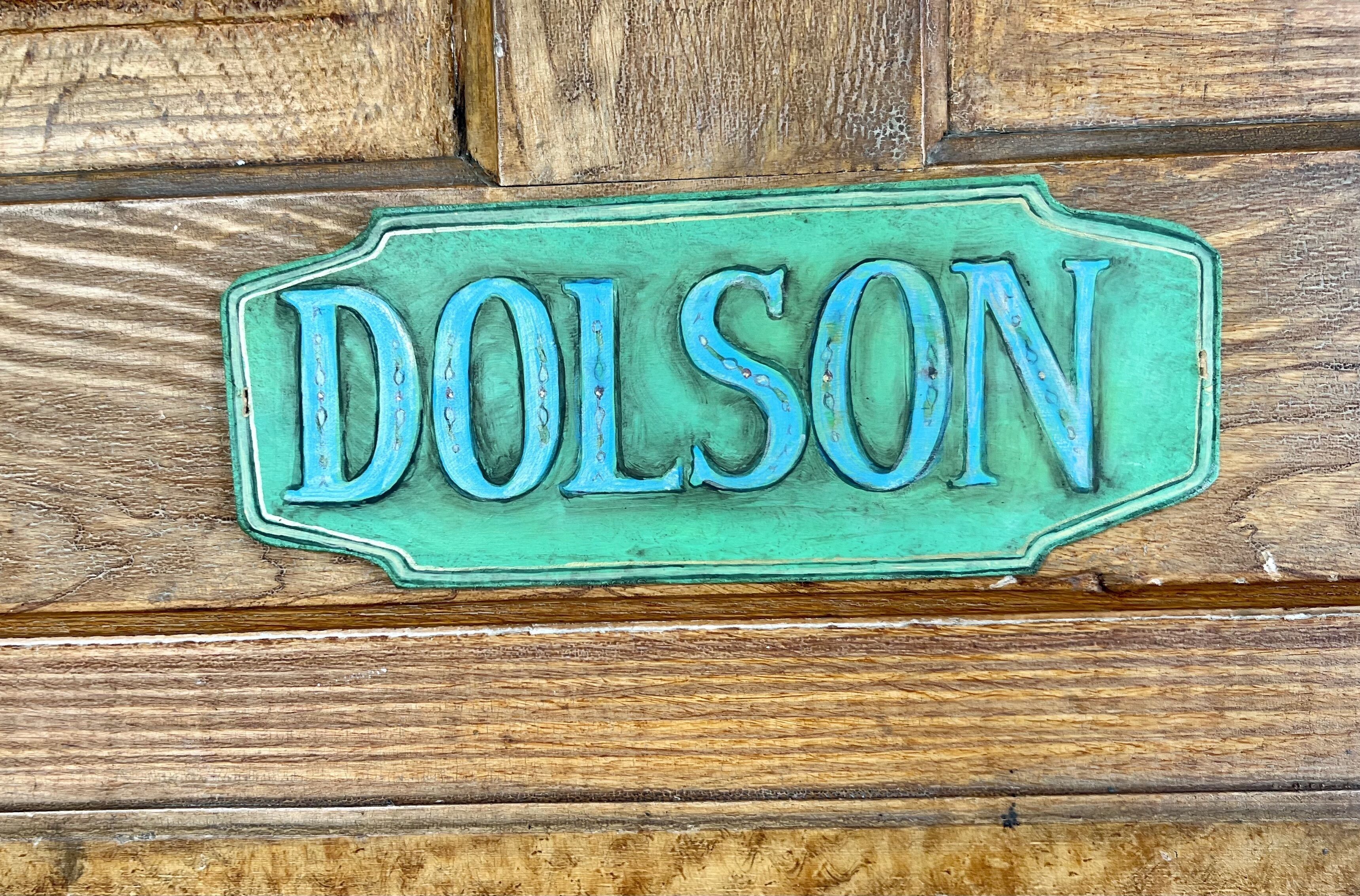 Un letrero de madera con el nombre "DOLSON" en letras mayúsculas.